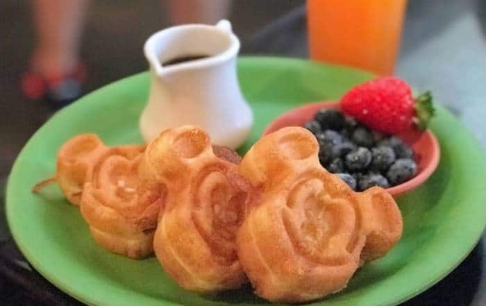 A plate with mini waffles in the shape of mickey with syrup and fresh fruit