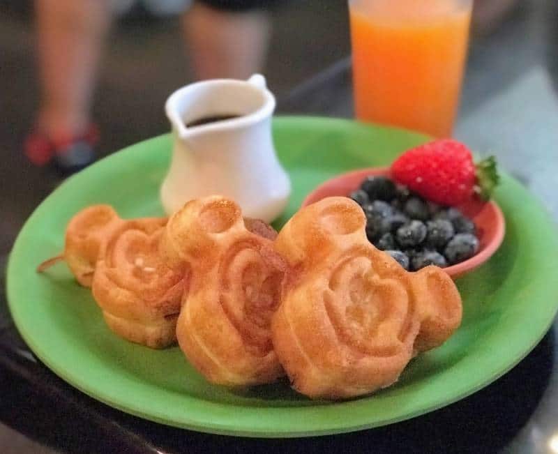 A plate with mini waffles in the shape of mickey with syrup and fresh fruit